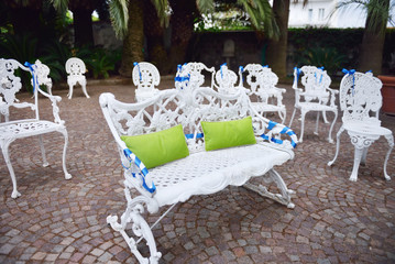 Setting for outdoor wedding ceremony with decorated chairs and bench for bride and groom