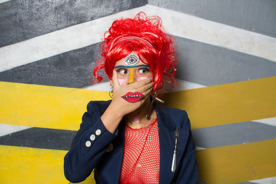 Retrato de chica joven con est&eacute;tica punk y post-punk (tribu urbana futurista) con peluca roja y con la cara pintada haciendo gestos provocativos