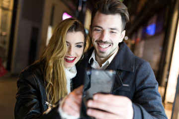 Beautiful young couple using they mobile phone in the street.