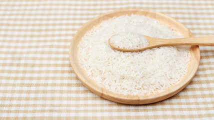 Spoon and Uncooked white rice on wooden plate 