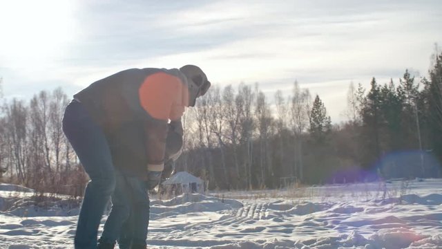 Father playing with kid in snowy park at winter day: he lifting him up and spinning around while mom looking at them and laughing