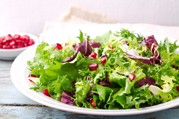 Green salad with spinach, frisee, arugula, radicchio and pomegranate seeds on blue wooden background