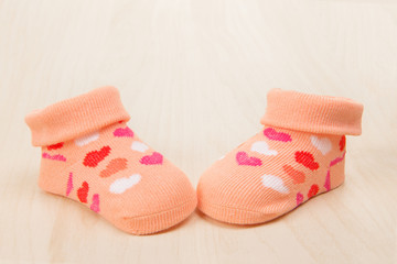 Pink baby sock with hearts on a wooden background