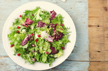 Green salad with spinach, frisee, arugula, radicchio and pomegranate seeds on blue wooden background