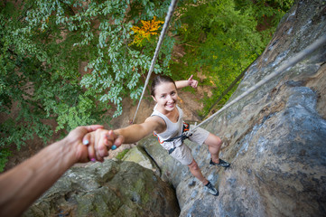Portrait of young happy woman climber giving thumb up and smiling on high rock. Partner giving a...