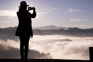 Fototapeta premium Silhouette of beautiful woman holding smartphone,take photo,happy and smile,with sunrise background,Ban Kong, Mae Hong Son, Thailand.