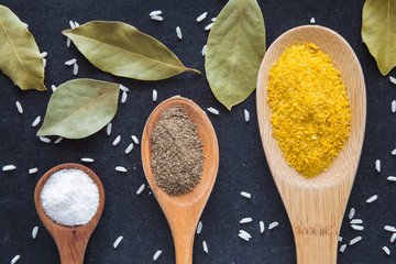Seasoning in the wooden spoons - white salt, ground pepper and yellow spice. Composition of seasoning on the dark background. Healthy eating and lifestyle.