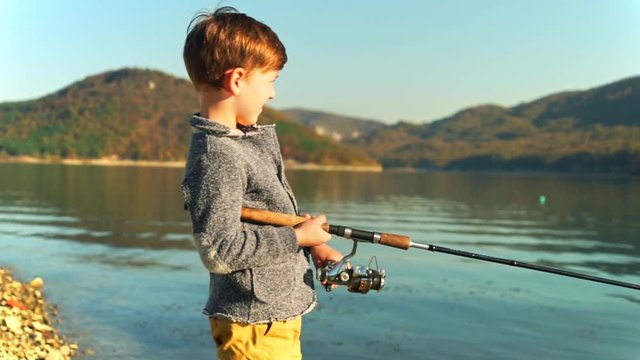 Blonde boy catches fish in the lake fishing rod bright sunny day close-up on a background of a beautiful mountain area