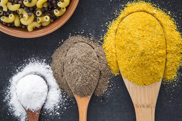 Seasoning in the wooden spoons - white salt, ground pepper and yellow spice. Composition of seasoning on the dark background. Healthy eating and lifestyle.