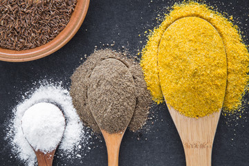 Seasoning in the wooden spoons - white salt, ground pepper and yellow spice. Composition of seasoning on the dark background. Healthy eating and lifestyle.