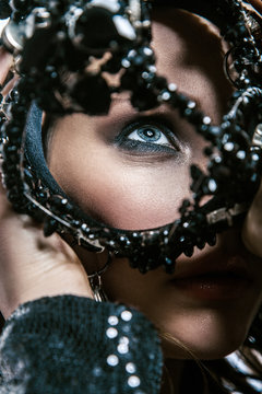 Fashion beauty portrait of young beautiful young woman with makeup, blue eyes and freckles on her face holding black crown in front of her face.
