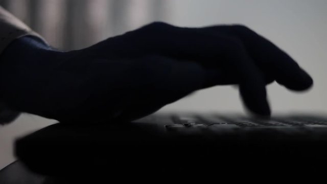 Shadow, silhouette of a male palm hand, typing on the laptop keyboard in the darkness.