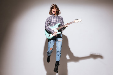 Attractive woman holding guitar over white background and jumping
