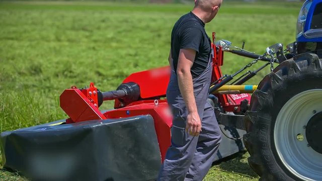 A young farmer is lifting up grass cutting machinery a few times which is connected to its tractor and then he goes back on a tractor.
