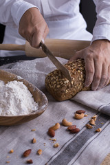 A male chef's hand present and cutting whole grain bread with gold knife and pouring flour.