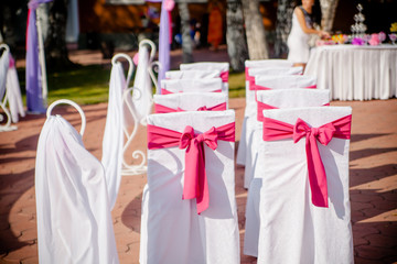 Close-up of white wedding chairs with purple ribbon