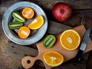 composition of the cut fruit, orange, kiwi, tangerine, pomegranate on a wooden board and a plate. Selective focus