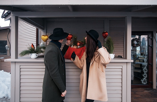 happy fashionable couple in winter green and beige coats and hats standing on terrace decorated by Christmas toys.Outdoor,beauty face,trendy outfit.hipsters smile.Winter holidays.British classic style