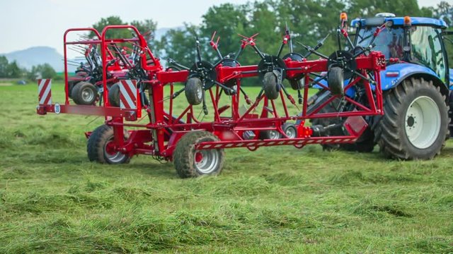 A farmer on a tractor is slowly opening rotary rakes and now, he will begin organizing freshly mowed lawn.
