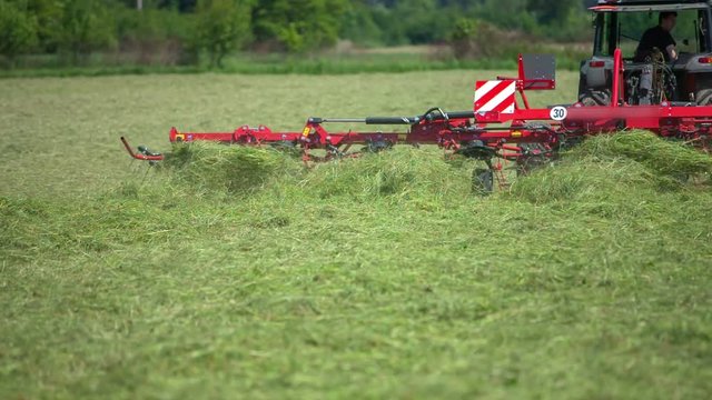 A tractor is slowly lowering down rotary hay rakes that are connected to the tractor. A farmer will now begin working on the fields with the mowed lawn.
