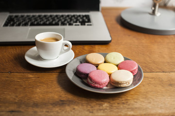 Obraz na płótnie Canvas Fresh morning espresso coffee and some french macarons dessert and a business laptop on the wooden table background