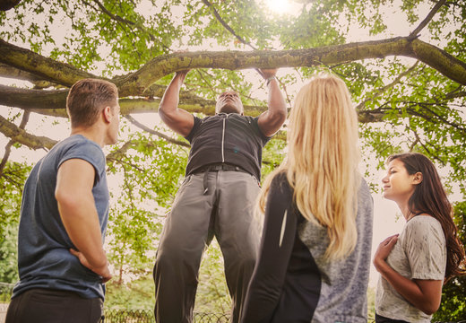 Personal trainer demonstrating pull ups on park tree branch
