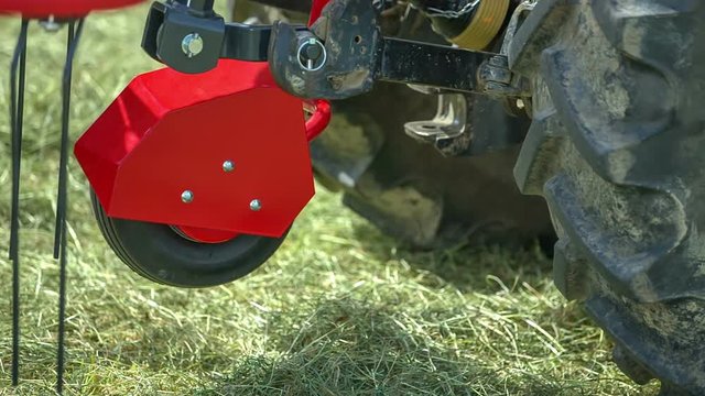 A trailer connector is moving up and then down again. A rotary hay rake is connected to the tractor because a farmer is preparing hay.
