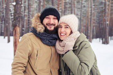 Fototapeta premium Cheer couple embracing over a picturesque wintry forest
