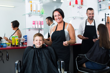 Cheerful female hairdresser cutting hair boy