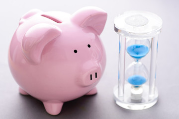 Piggy bank near classic hourglass with blue sand