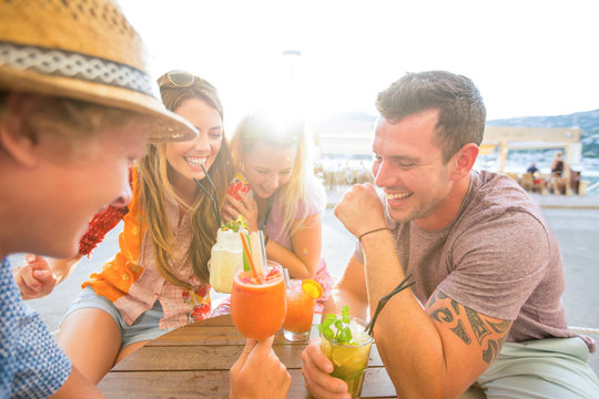 Two adult couples laughing over cocktails at waterfront restaurant, Majorca, Spain