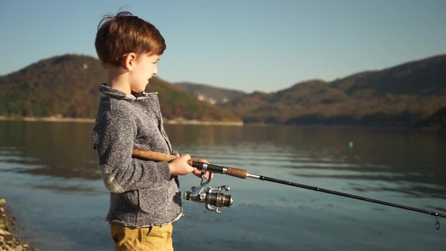 Blonde boy catches fish in the lake fishing rod bright sunny day close-up on a background of a beautiful mountain area