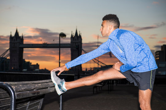 Man stretching by riverside, Tower Bridge in background, Wapping, London, UK