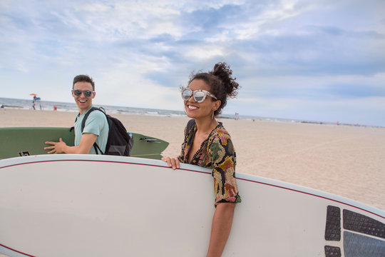 Young couple carrying surfboards on Rockaway Beach, New York State, USA