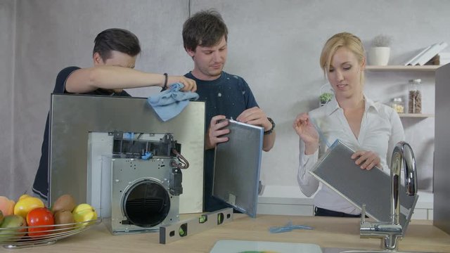 A few people are standing behind a counter in the kitchen and they are cleaning the kitchen hood parts.
