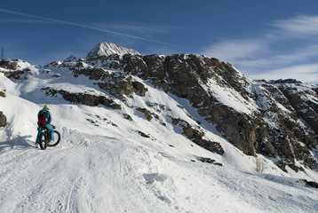 Fototapeta na wymiar Sciatore con ebike - mountain bike elettrica - fat bike da neve, che sale in alta montagna con gli sci caricati sulla bici, Riale, Val Formazza, Ossola, Alpi Italia