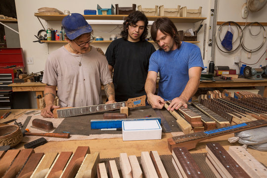 Guitar makers in workshop quality checking guitar necks
