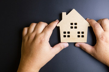 Man's hand holding wooden house toy on black background with cop