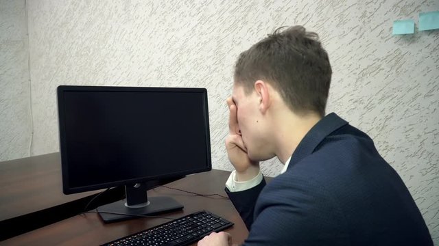 Young man suffering from headache working on computer in the office