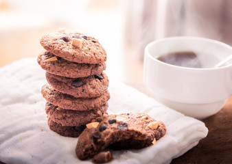 Chocolate chip cookies on napkin and hot tea on wooden table.