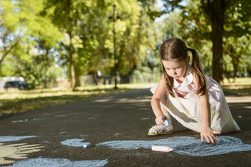 Little girl drawing on asphalt with chalk in a sunny summer day. Concept of child imagination