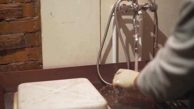 Man washes a piece of glass under the water in the sink