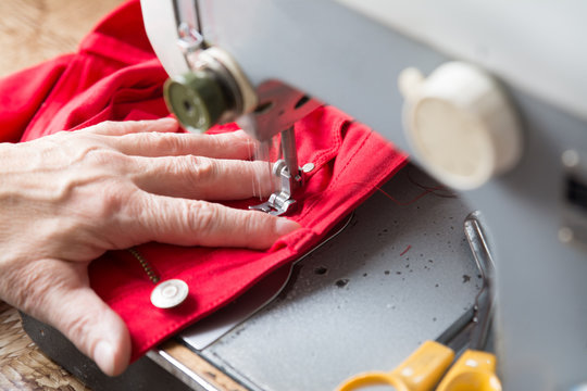 Older Woman Si Fixing Red Jeans On A Sewing Machine.