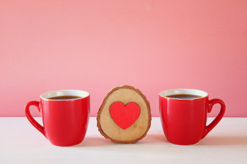 Wooden heart next to coffee cups on wooden table