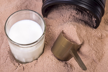 Macro image of protein for fitness and bodybuilding. Black jar with whey caramel protein. Scoop full of protein near the jar. Glass full with milk staying on the heap of protein.