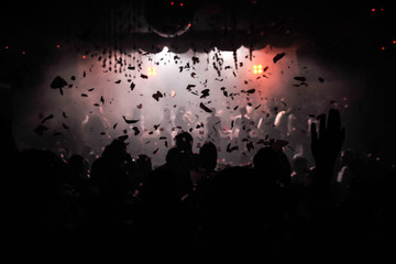 Confetti fired on air during a party in a disco. Confetti for background. Silhouette of happy people on dancefloor. Hands are in the air