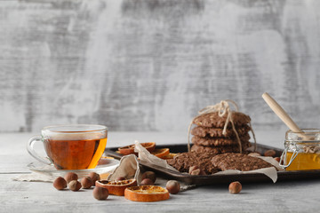 Fresh oat cookies with honey and cup of tea on white table