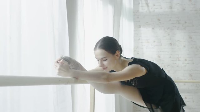 Young and Beautiful Ballerina Doing Leg Stretching at the Barre. Shot on a Sunny Morning in a Spacious and Light Studio. In Slow Motion. Shot on RED EPIC-W 8K Helium Cinema Camera.