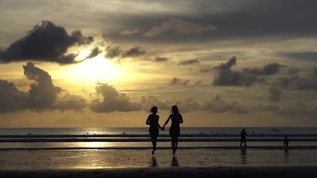 two young women lesbians fleeing from the ocean at sunset