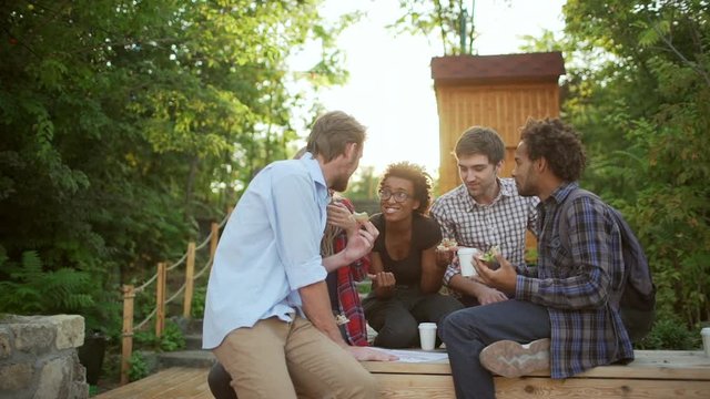 Interracial female and male friends sitting smiling talking chatting eating pizza in park in slowmotion